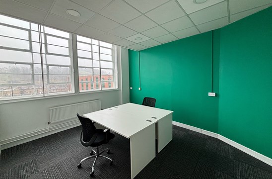 Office 319 with a large window, green feature wall and a desk.